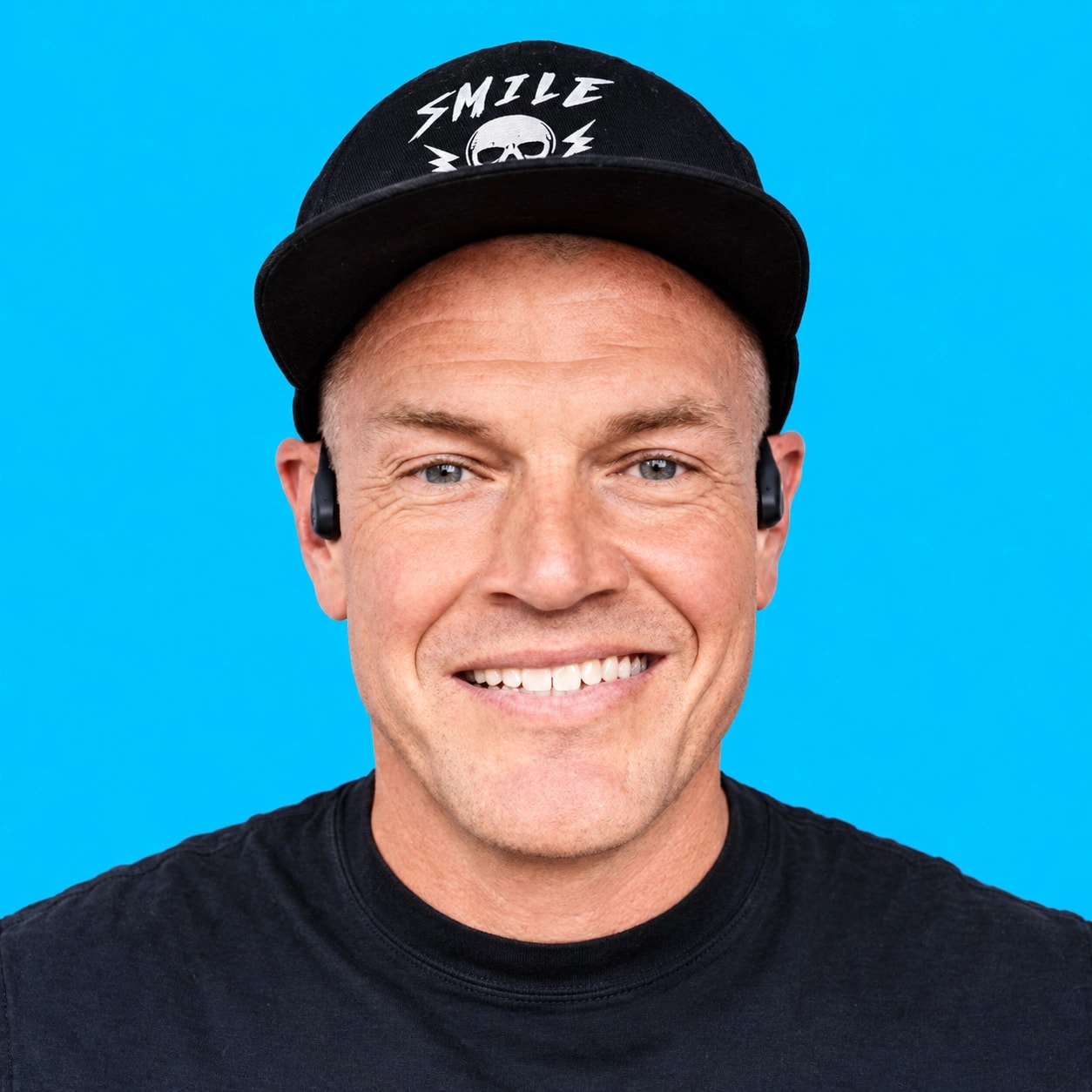 Andy Glaze smiling in his black cap against a bright blue background